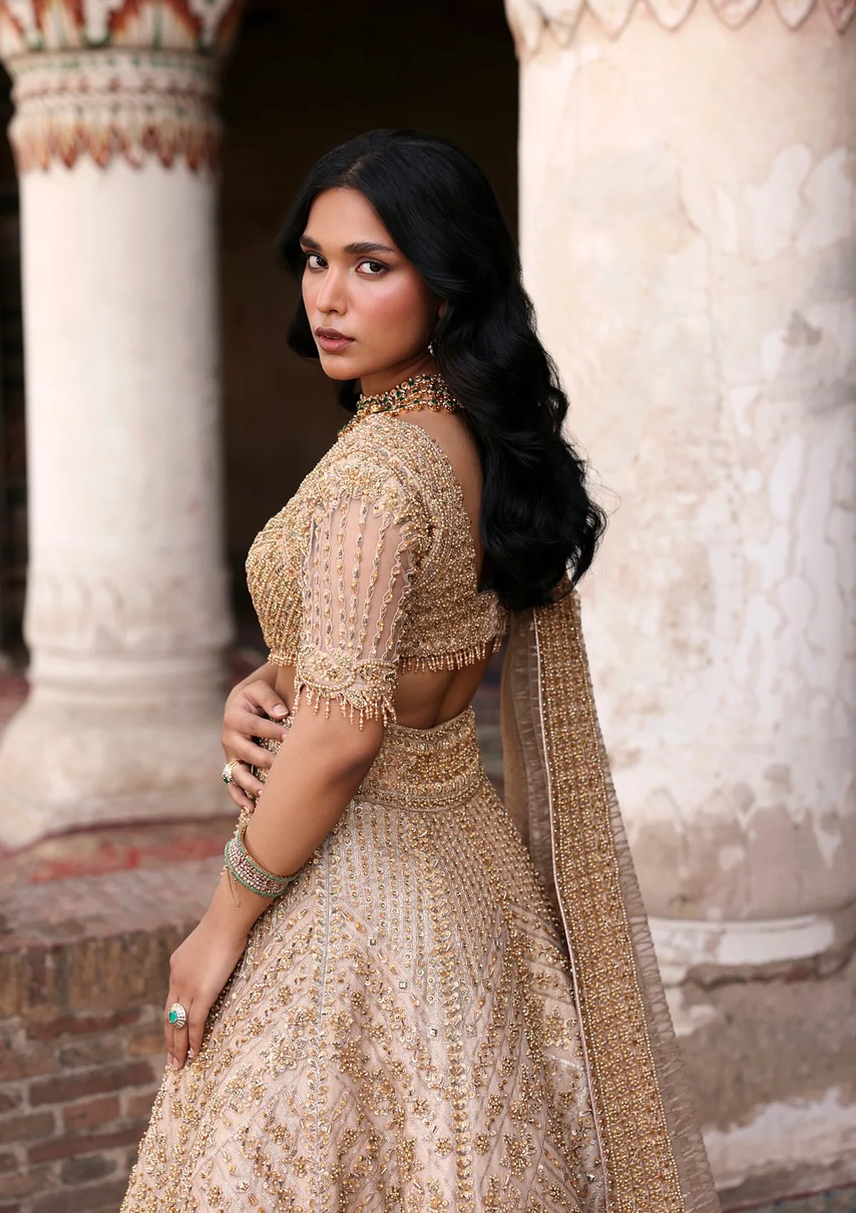 A gold embroidered lehenga photographed between stone pillars