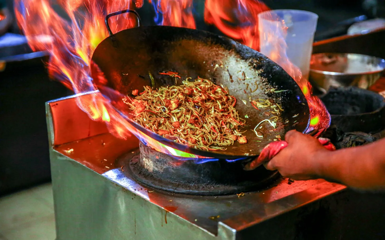A chef tossing noodles in a flaming wok